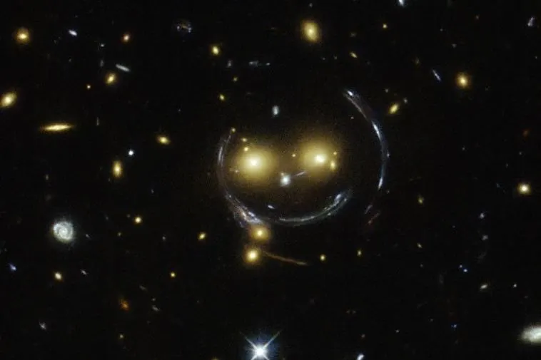 A ring of light bent into a smile shape around two glowing galaxies in a Hubble image of a galaxy cluster