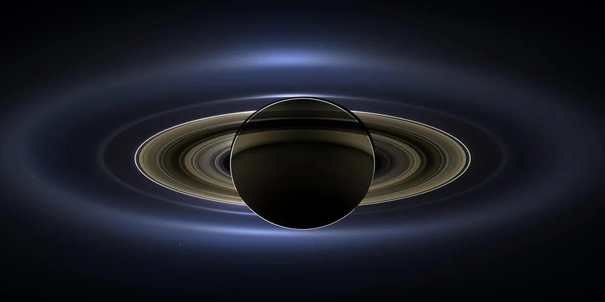 Saturn eclipsing the Sun, with glowing rings and a tiny Earth in the distance