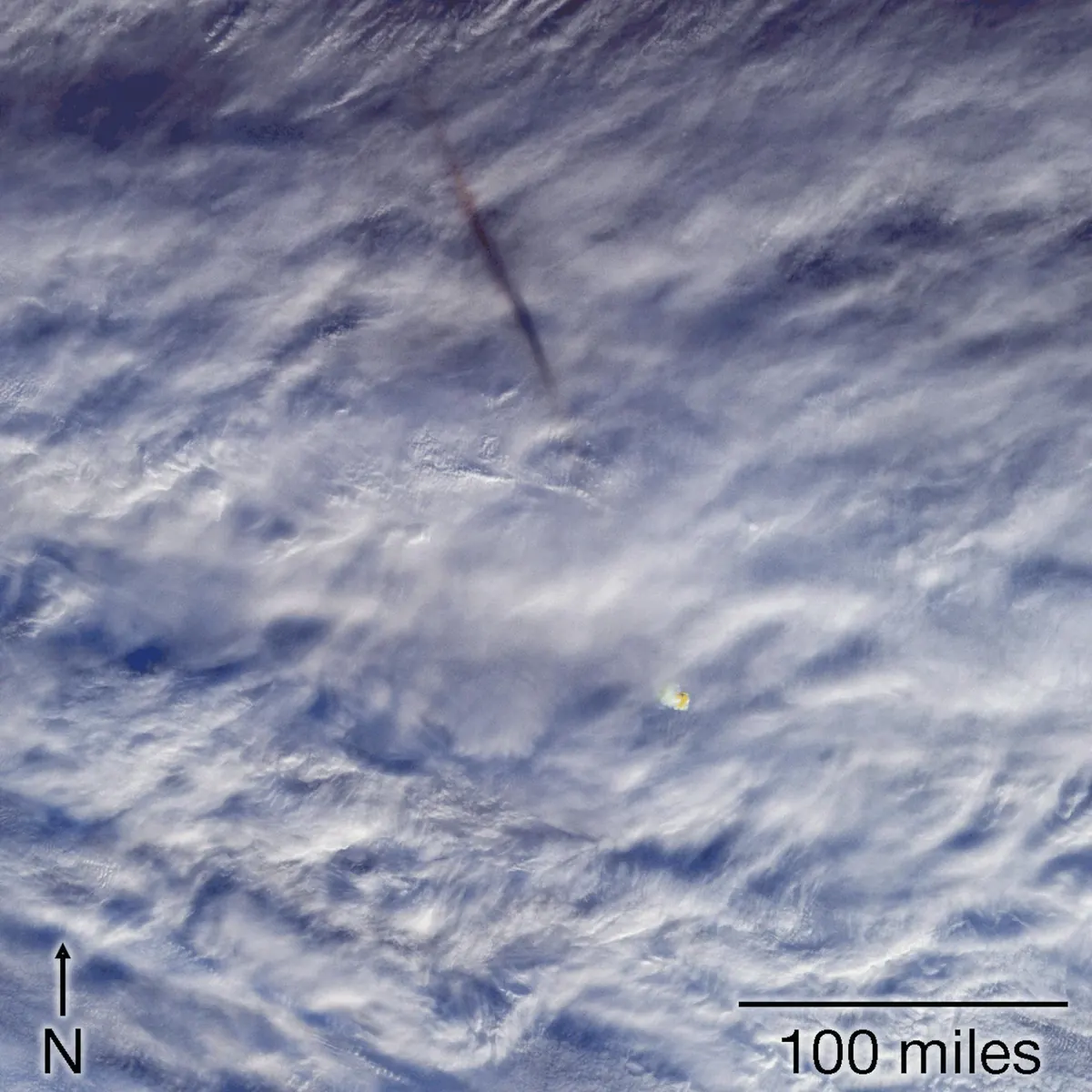 A satellite view of cloud tops with a thin dark streak left by a fireball