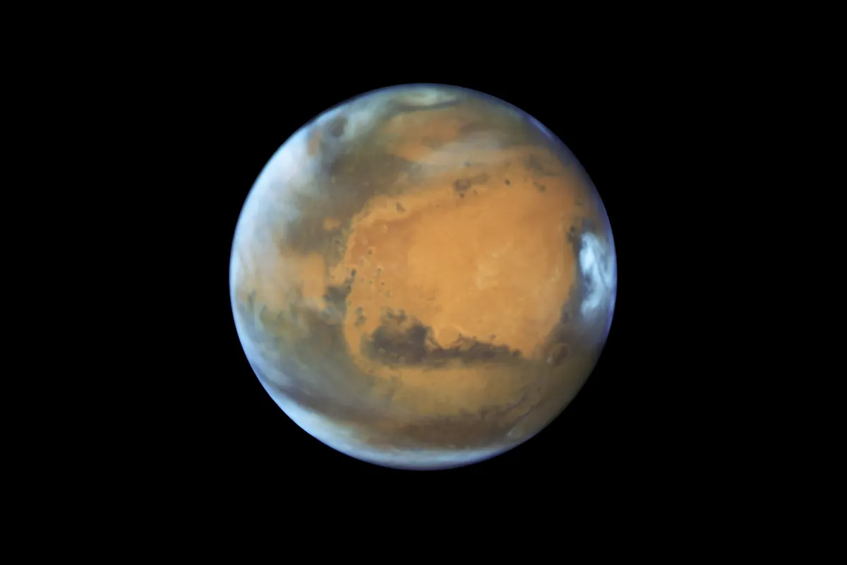 Mars as a rust-colored disc with a bright polar cap and dark surface markings, seen by the Hubble Space Telescope