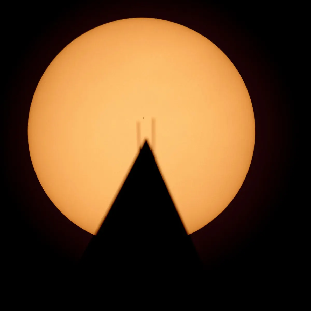 The Sun as a bright disc behind the pointed tip of the Washington Monument, with the tiny dark dot of Mercury crossing its face