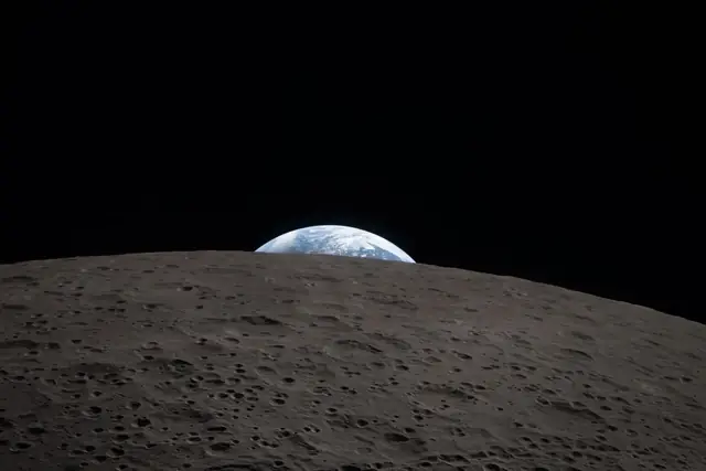Earth setting behind the gray, cratered horizon of the Moon