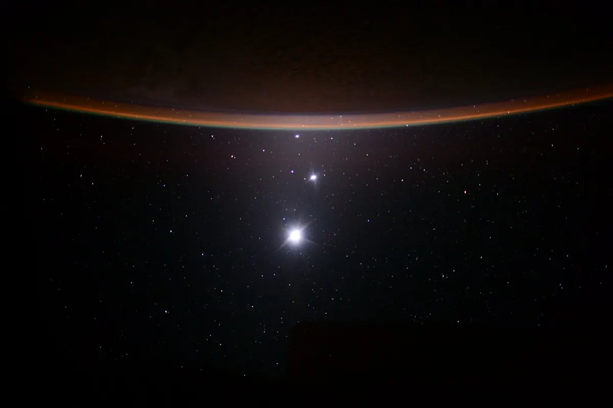 The Moon, Venus and Jupiter as bright points above the curved glow of Earth's horizon