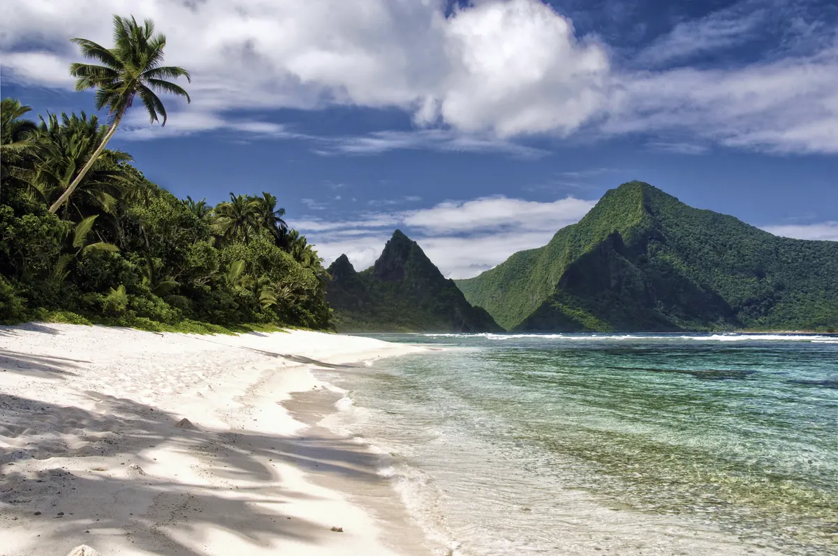 A white sand beach, palm trees and green volcanic peaks on Ofu Island, American Samoa