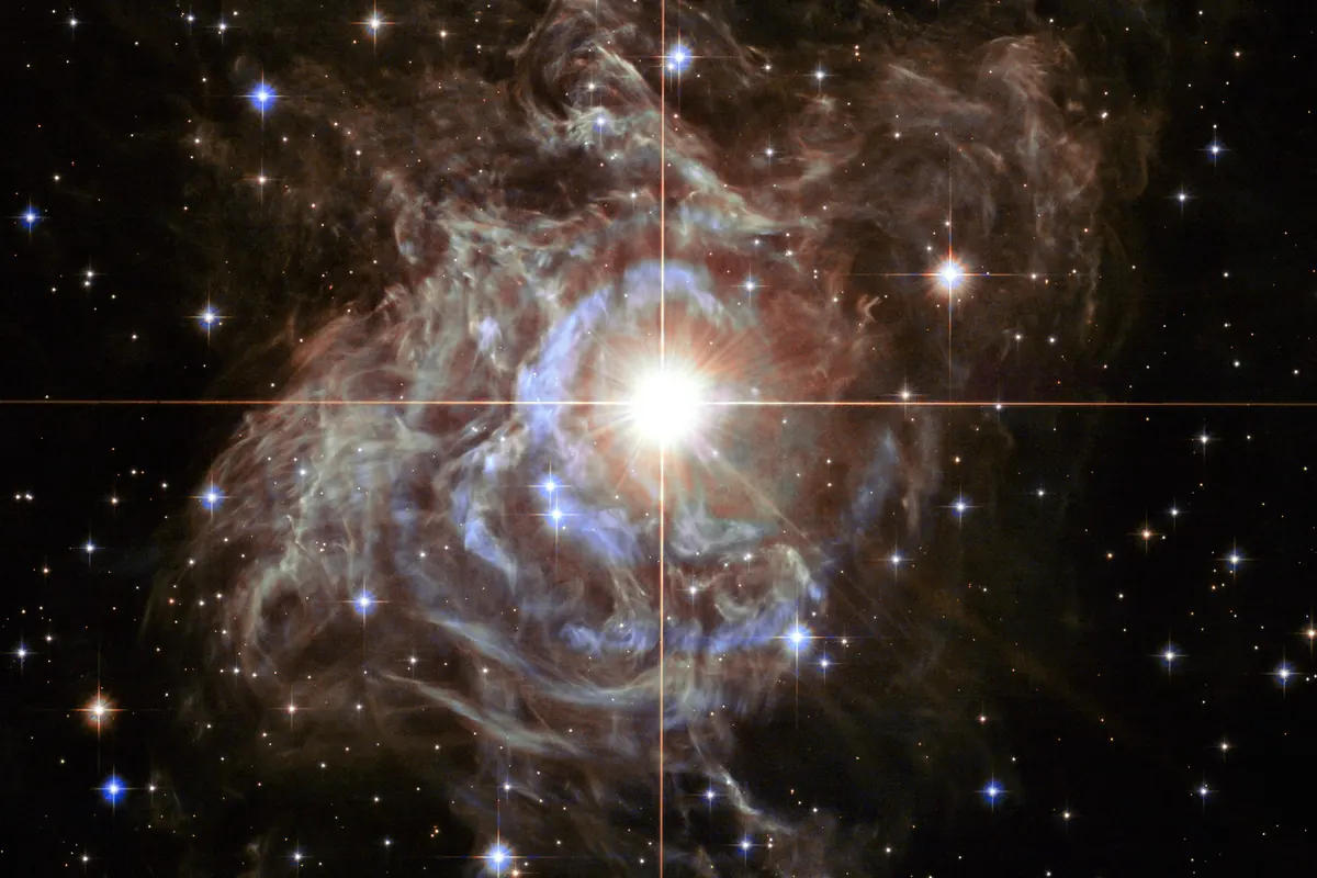 A star surrounded by a glowing cocoon of dust, with a faint cross of light spikes through its center