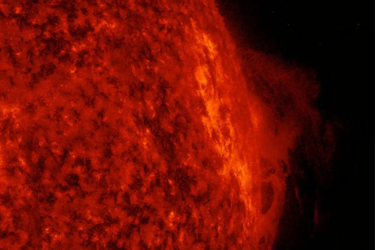 A bright red prominence of gas rising from the edge of the Sun
