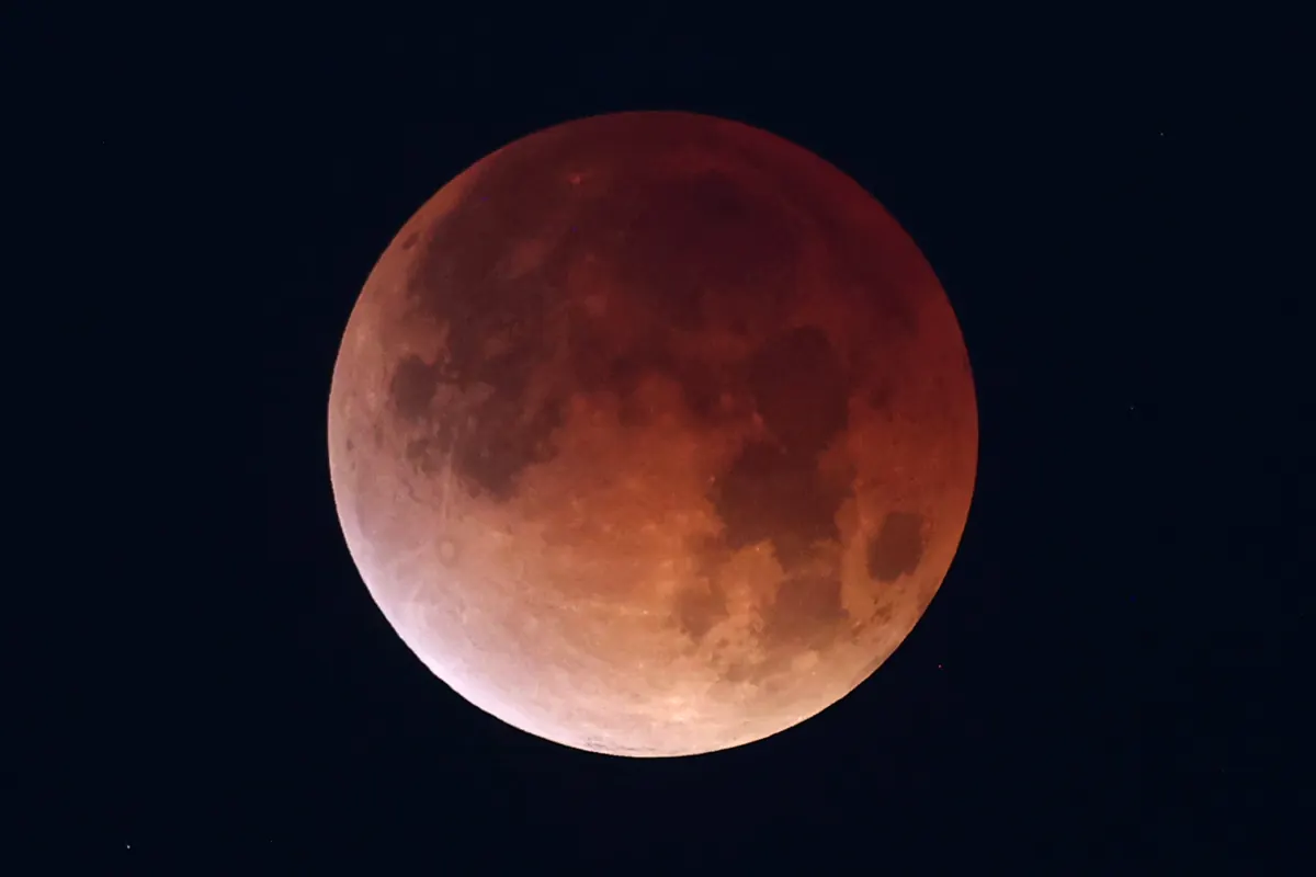A full Moon glowing deep red-brown against a dark blue sky during a total lunar eclipse